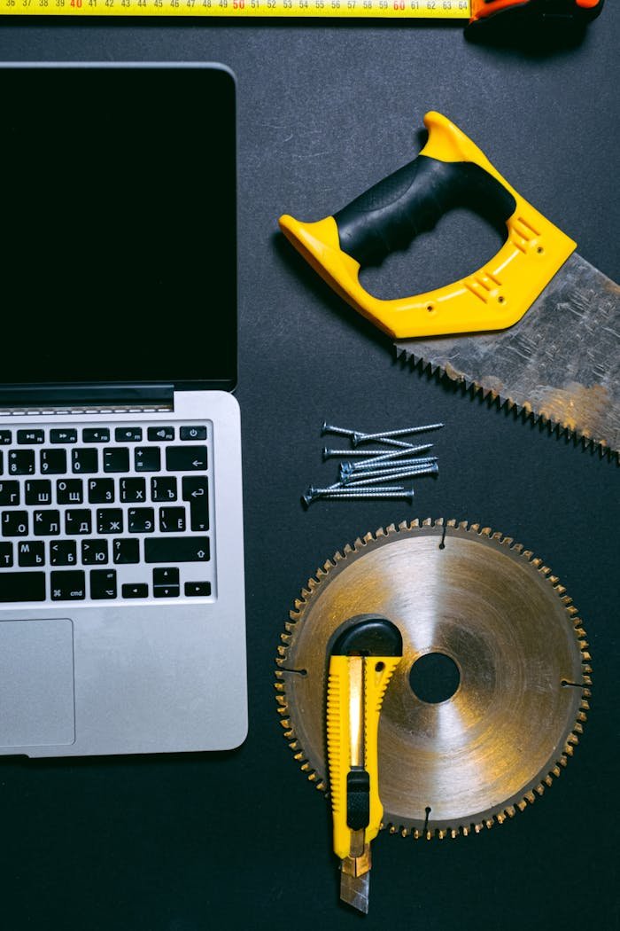 Flat lay of a laptop and various hand tools on a dark surface, perfect for DIY or technology themes.